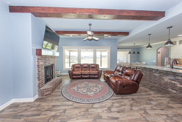 living room with beam ceiling, a brick fireplace, ceiling fan, and sink