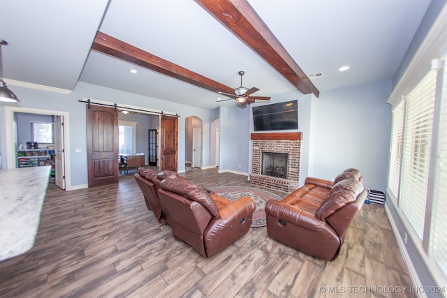 living room with beam ceiling, a barn door, hardwood / wood-style floors, and a healthy amount of sunlight