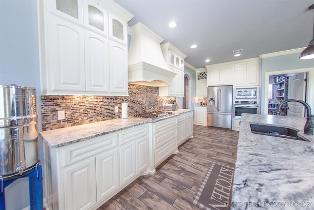 kitchen with sink, premium range hood, appliances with stainless steel finishes, white cabinets, and ornamental molding