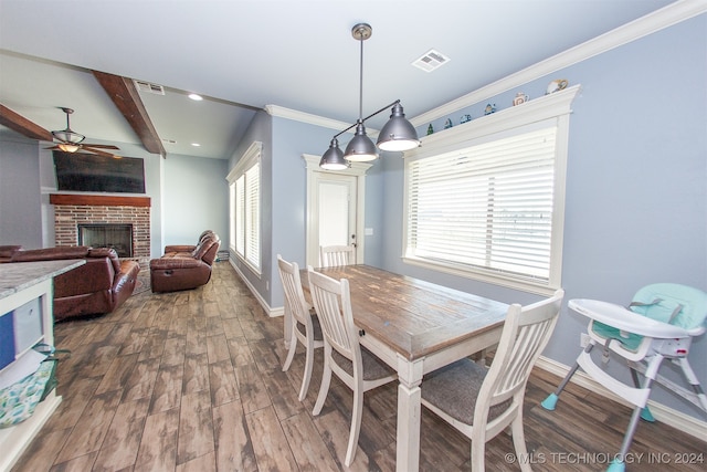 dining area featuring dark wood-type flooring, a brick fireplace, ceiling fan, ornamental molding, and beam ceiling