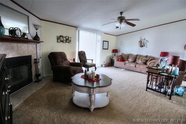 living room featuring dark colored carpet, ceiling fan, crown molding, and a tiled fireplace