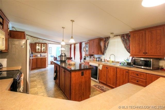 kitchen featuring a center island, sink, vaulted ceiling, appliances with stainless steel finishes, and decorative light fixtures