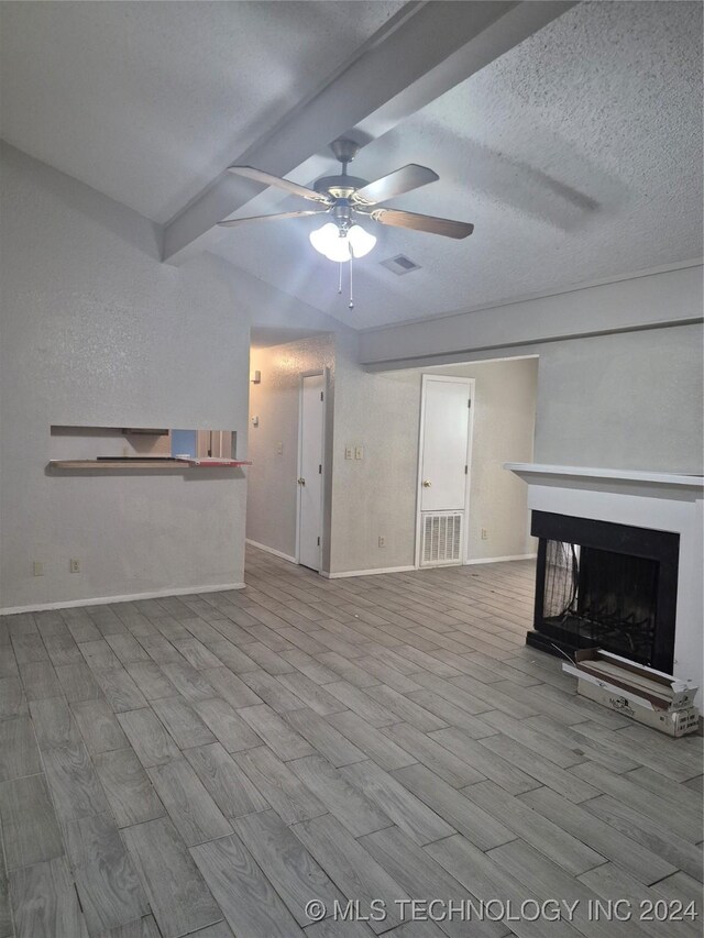 unfurnished living room with a textured ceiling, ceiling fan, beamed ceiling, a multi sided fireplace, and light hardwood / wood-style floors