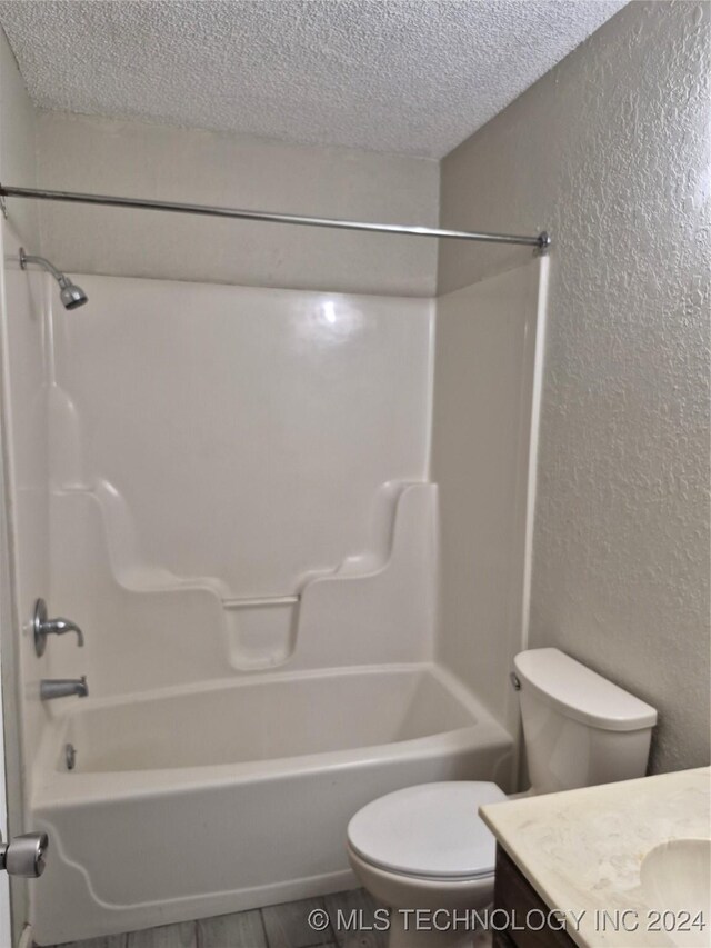 full bathroom featuring  shower combination, vanity, a textured ceiling, and toilet