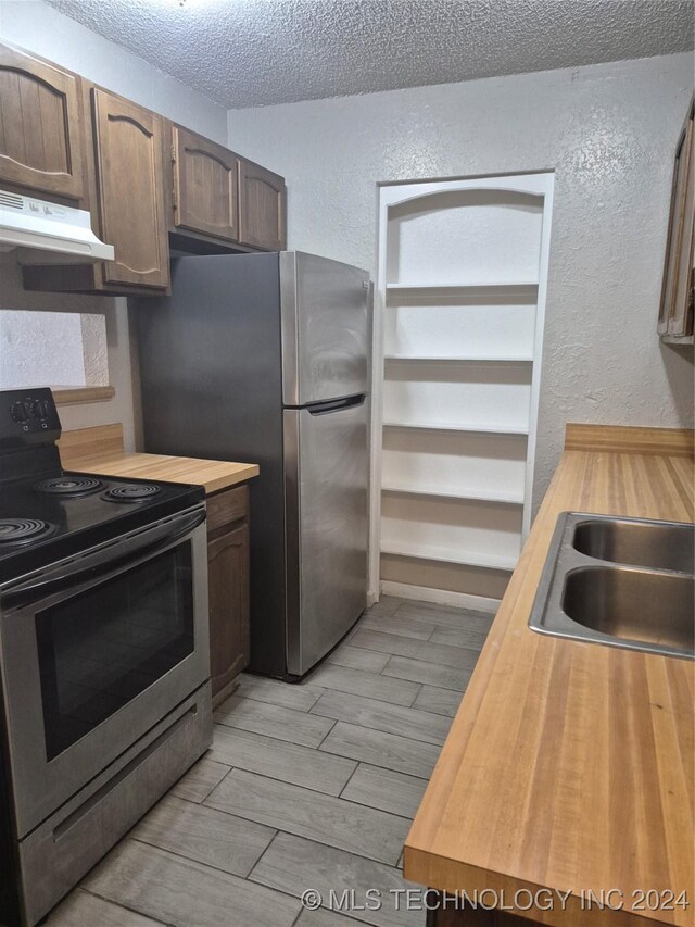 kitchen with sink, wooden counters, light hardwood / wood-style floors, a textured ceiling, and appliances with stainless steel finishes