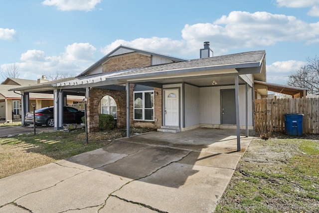 view of front of property with roof with shingles, fence, a carport, and brick siding