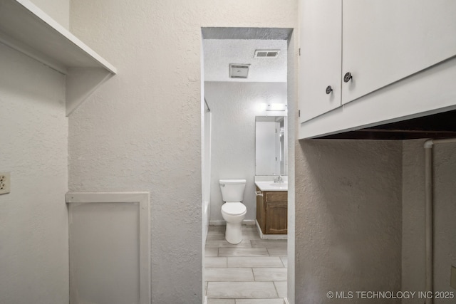 bathroom with toilet, a textured wall, visible vents, and vanity