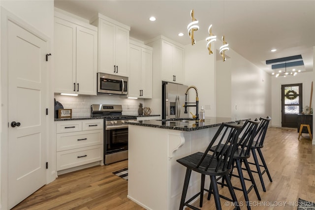 kitchen featuring dark stone counters, a center island with sink, sink, appliances with stainless steel finishes, and a breakfast bar area