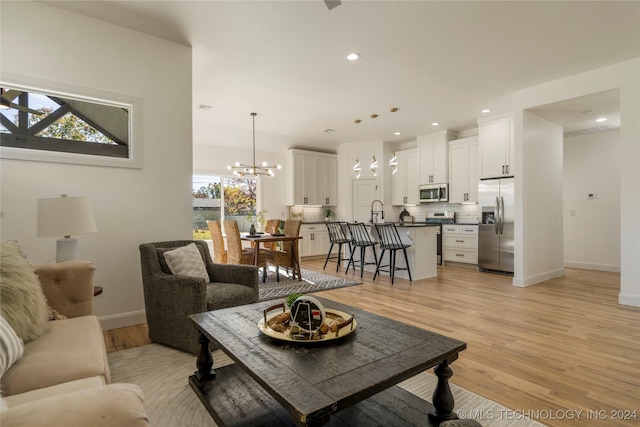 living room featuring sink, a healthy amount of sunlight, light wood-type flooring, and a notable chandelier