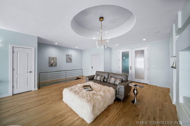 living room featuring a notable chandelier, a raised ceiling, and light hardwood / wood-style flooring