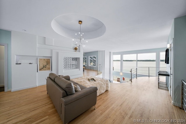 living room with a raised ceiling, light hardwood / wood-style floors, a water view, and a chandelier