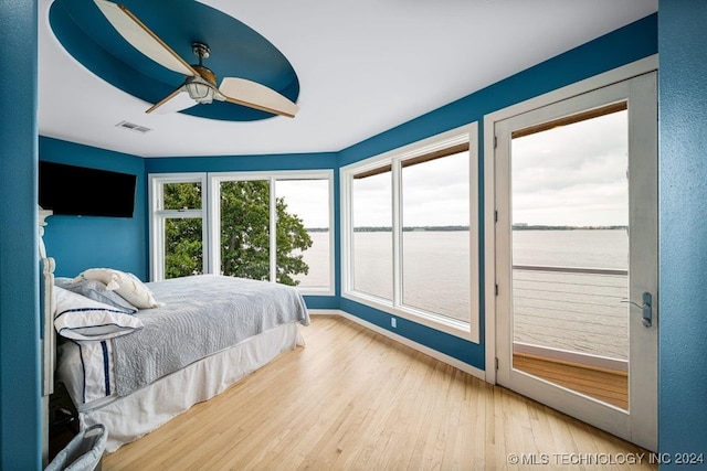 bedroom featuring access to exterior, hardwood / wood-style floors, a water view, and ceiling fan