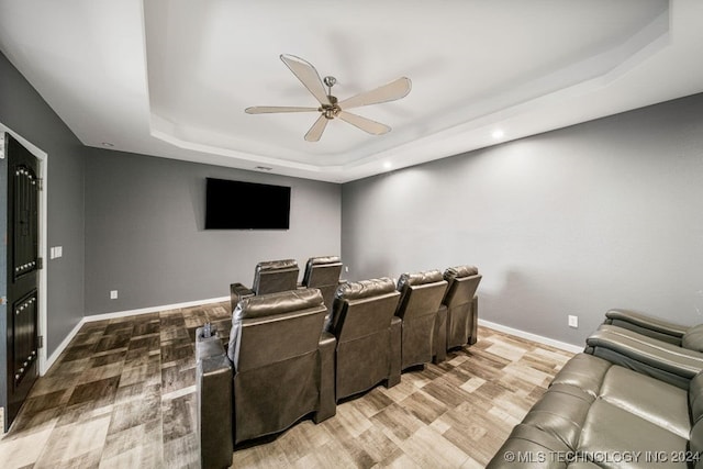 cinema with hardwood / wood-style flooring, ceiling fan, and a raised ceiling