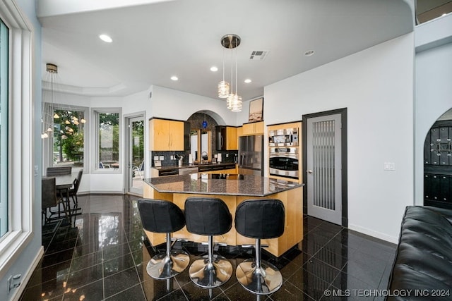 kitchen with pendant lighting, light brown cabinets, backsplash, appliances with stainless steel finishes, and a kitchen island