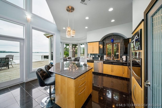 kitchen with sink, stainless steel appliances, a kitchen island, backsplash, and a water view