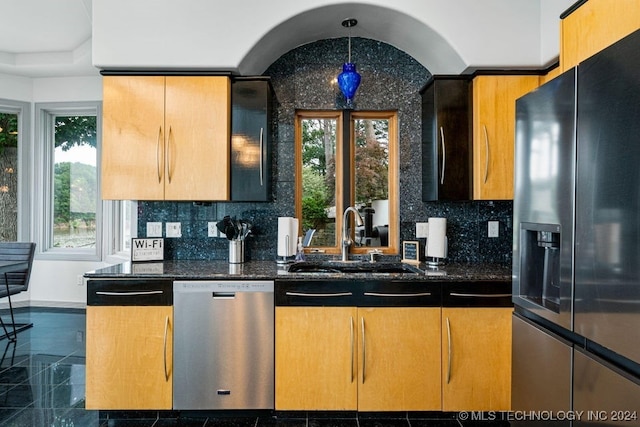 kitchen featuring stainless steel dishwasher, a wealth of natural light, black refrigerator with ice dispenser, sink, and dark stone countertops