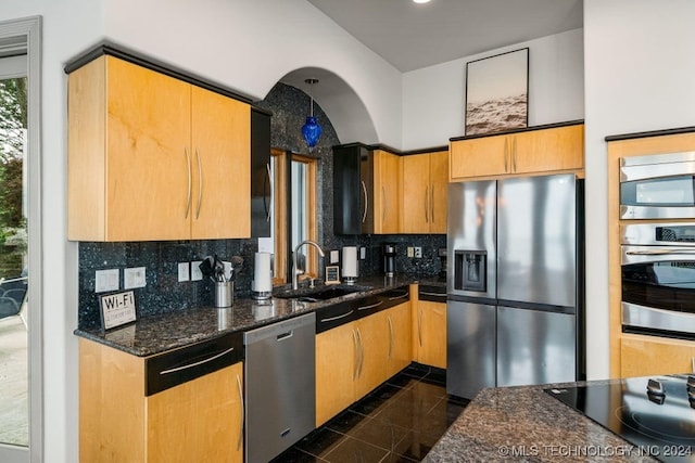 kitchen featuring appliances with stainless steel finishes, sink, backsplash, and dark stone countertops