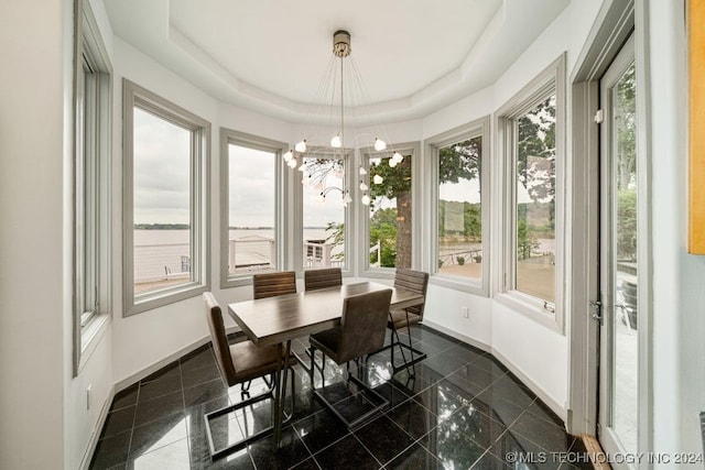 sunroom with a notable chandelier, a raised ceiling, and a water view