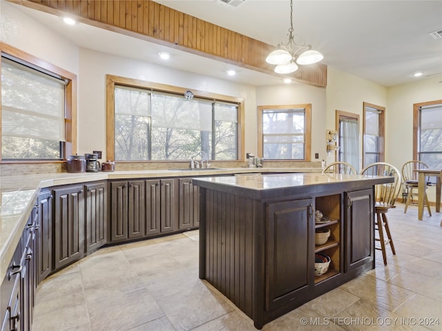 kitchen with a breakfast bar, decorative light fixtures, a notable chandelier, a kitchen island, and dark brown cabinets