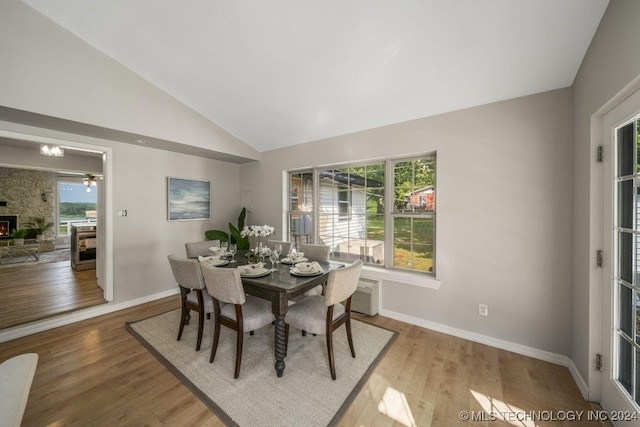 dining area with a wood stove, vaulted ceiling, and light hardwood / wood-style flooring