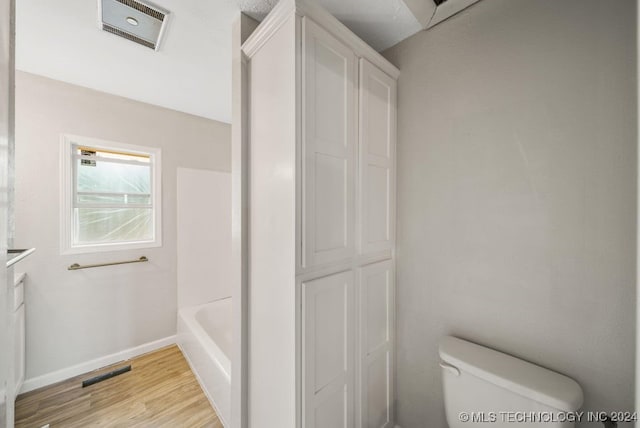 bathroom featuring a bathing tub, hardwood / wood-style floors, and toilet