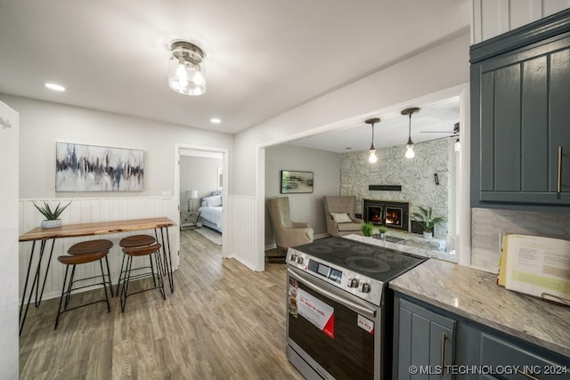 kitchen with light stone counters, electric range, decorative light fixtures, hardwood / wood-style floors, and a wood stove