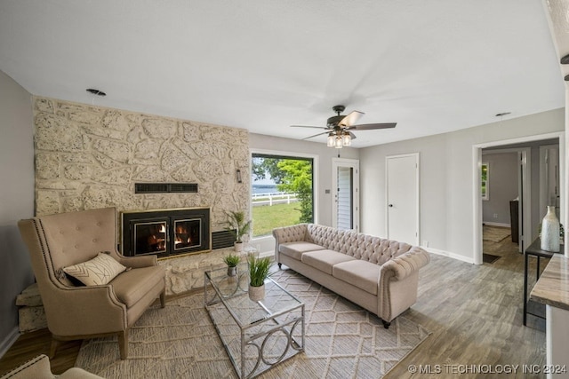 living room with ceiling fan, a stone fireplace, and wood-type flooring