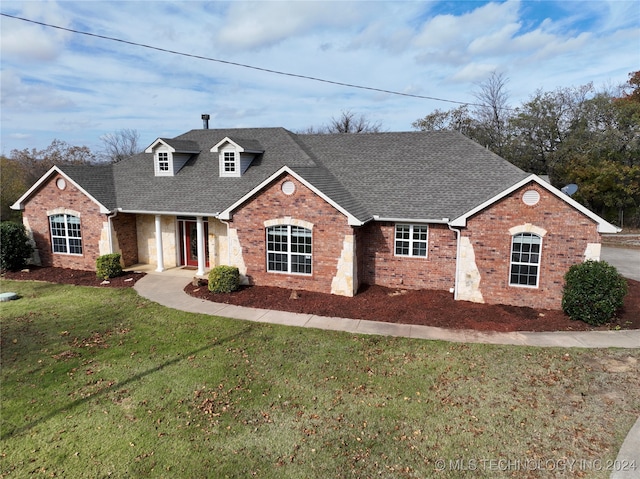 view of front facade with a shingled roof, brick siding, and a front yard
