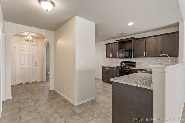 kitchen featuring backsplash, black appliances, a notable chandelier, light stone counters, and dark brown cabinetry