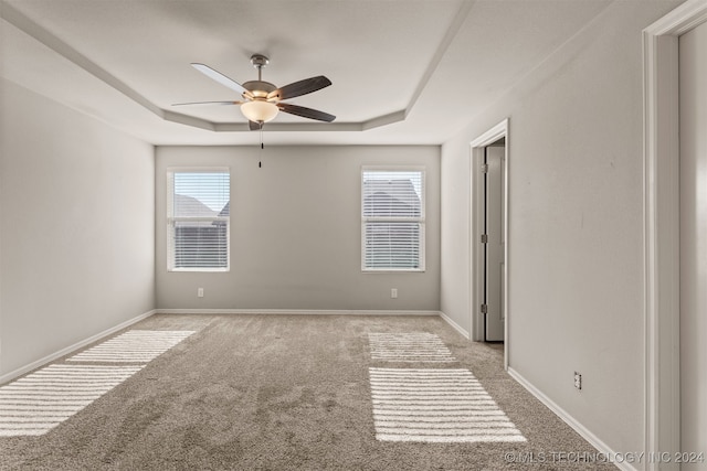 carpeted spare room featuring a raised ceiling and ceiling fan