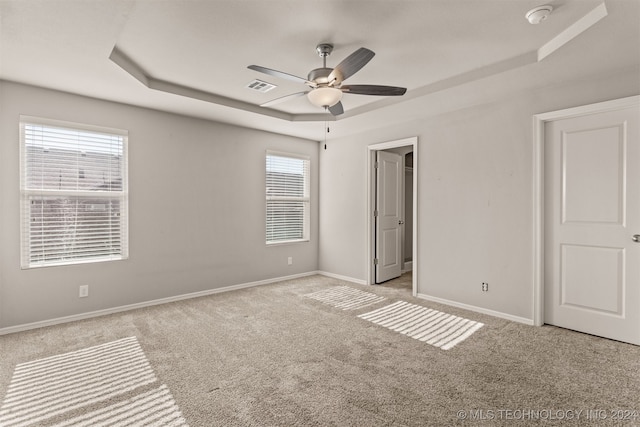 unfurnished bedroom with ceiling fan, a raised ceiling, and multiple windows