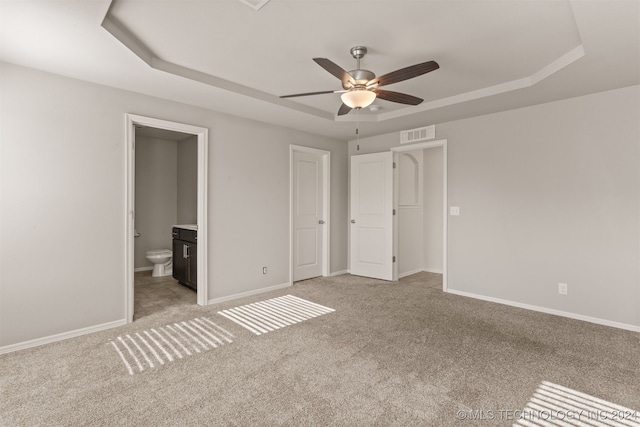 unfurnished bedroom featuring light carpet, ensuite bathroom, a raised ceiling, and ceiling fan