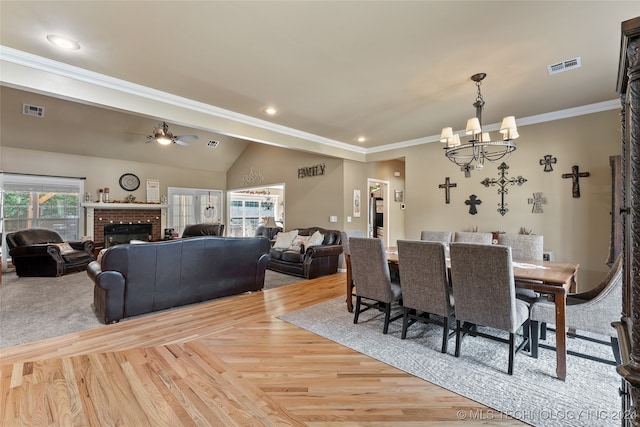 dining room with a brick fireplace, hardwood / wood-style floors, ceiling fan with notable chandelier, and ornamental molding