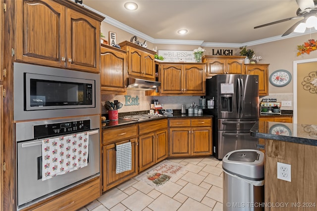 kitchen with ceiling fan, stainless steel appliances, crown molding, dark stone counters, and decorative backsplash