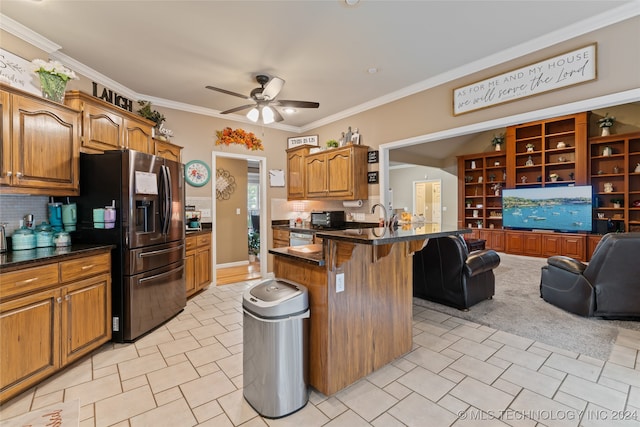 kitchen featuring ceiling fan, ornamental molding, an island with sink, a kitchen bar, and stainless steel fridge with ice dispenser