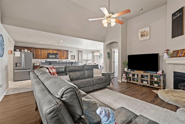 living room featuring a fireplace, hardwood / wood-style floors, ceiling fan with notable chandelier, and lofted ceiling