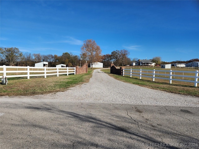 view of street with a rural view and gravel driveway