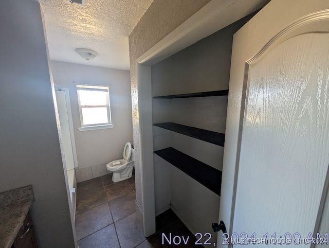 bathroom with tile patterned flooring, vanity, toilet, and a textured ceiling