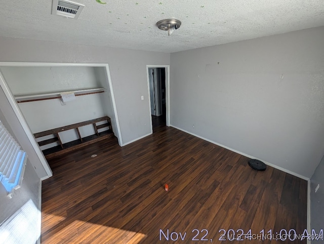 unfurnished bedroom featuring a textured ceiling, dark hardwood / wood-style flooring, and a closet