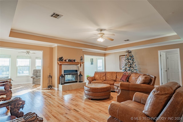 living room with a tiled fireplace, wood-type flooring, ceiling fan, and a tray ceiling