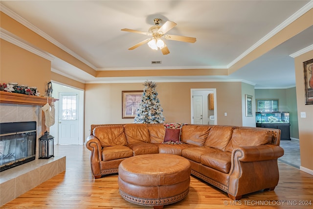 living room with crown molding, a fireplace, ceiling fan, and light wood-type flooring