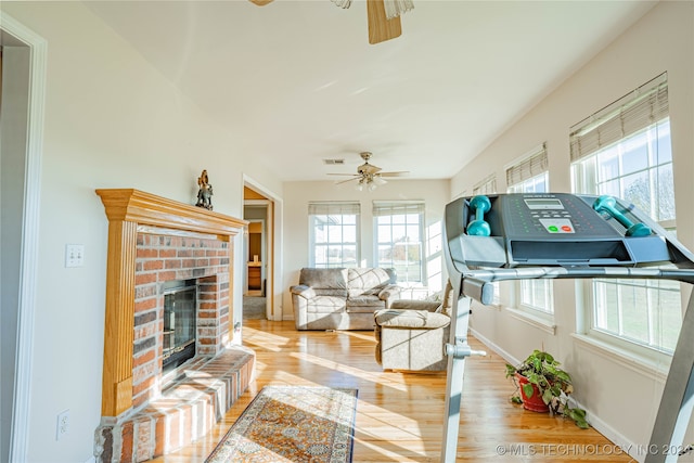 living room with a brick fireplace, ceiling fan, and light hardwood / wood-style flooring