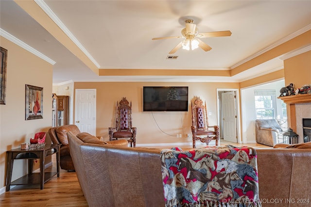 living room with crown molding, light hardwood / wood-style flooring, ceiling fan, a tray ceiling, and a fireplace