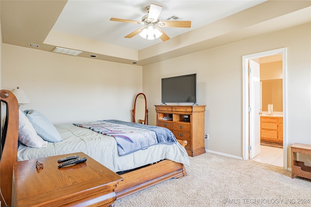 carpeted bedroom featuring ceiling fan, ensuite bath, and a tray ceiling