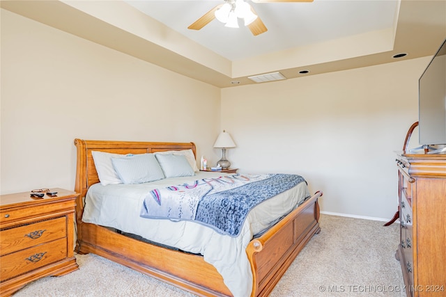 bedroom with light carpet, a tray ceiling, and ceiling fan