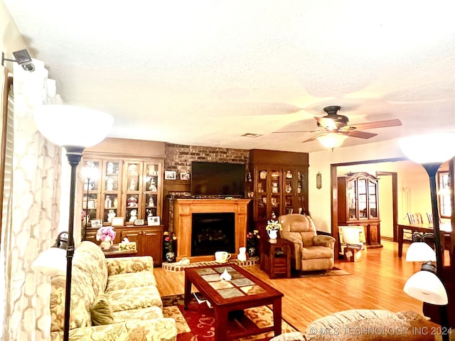 living room with a brick fireplace, ceiling fan, a textured ceiling, and hardwood / wood-style flooring