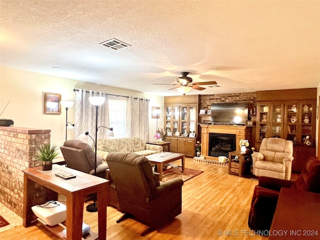 living room featuring hardwood / wood-style floors, a textured ceiling, a brick fireplace, and ceiling fan