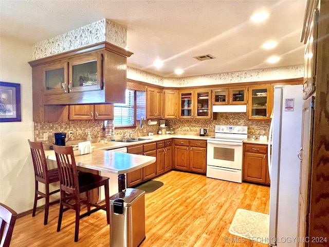 kitchen with kitchen peninsula, a textured ceiling, white appliances, and light hardwood / wood-style floors