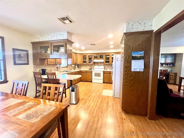 kitchen with backsplash, light hardwood / wood-style floors, white appliances, and a textured ceiling