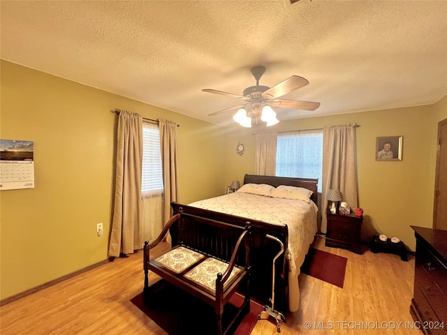 bedroom with a textured ceiling, ceiling fan, light hardwood / wood-style flooring, and multiple windows